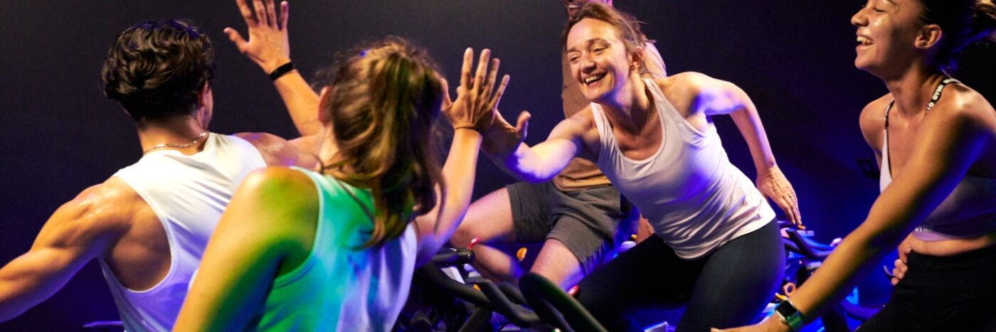 groupe de personne souriantes se tapant dans les mains après une séances de RPM dans une salle L'Appart Fitness