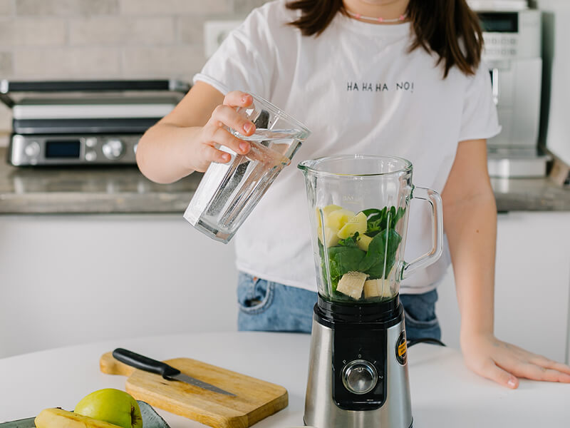 Une femme en train de réaliser un jus détox dans sa cuisine - Conseils détox