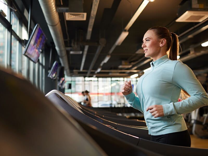 Jeune femme en train de courir sur un tapis de course dans une salle de sport