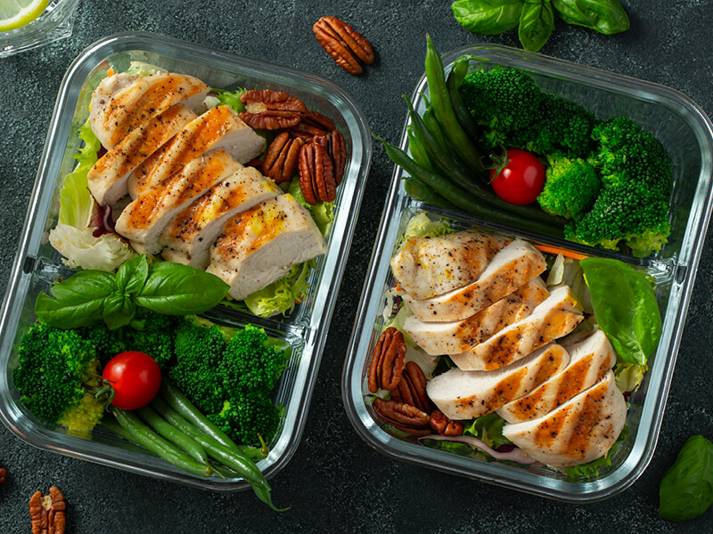 2 lunch boxes de poulet, légumes verts et noix pour illustrer un article sur le rééquilibrage alimentaire
