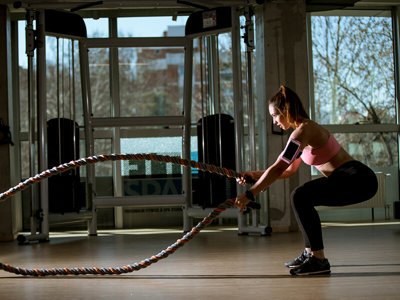 Une femme en train de s'entrainer avec une battle rope lors d'une séance de cross training dans une salle de fitness