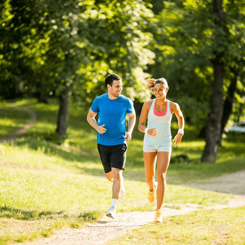 Un homme et une femme courant dans un parc, montrant la préparation pour courir son premier 10km avec L'Appart Fitness.