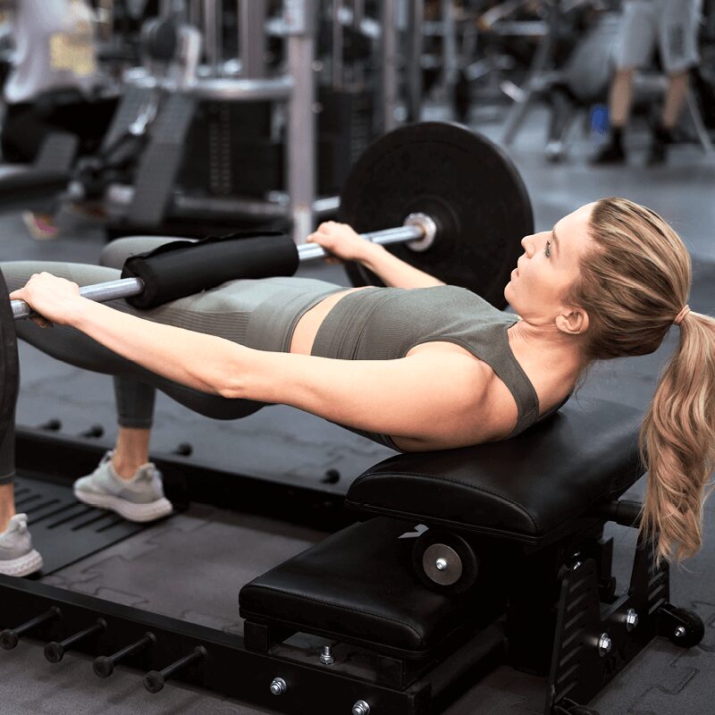 Une femme réalisant un hip thrust avec barre, un exercice bas du corps proposé par L'Appart Fitness pour renforcer les fessiers.