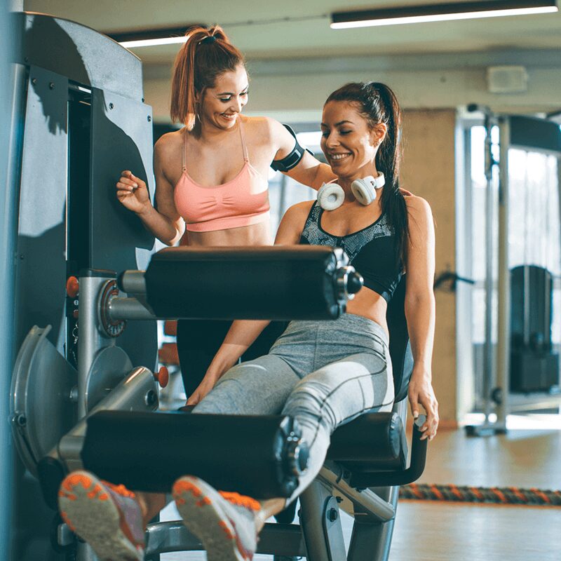 Deux femmes pratiquant la leg extension à la salle, un exercice bas du corps essentiel selon L'Appart Fitness.