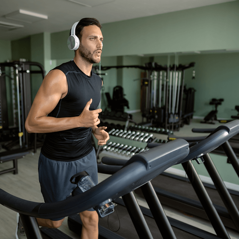 Un homme courant sur un tapis de course en salle de sport, mettant en valeur les équipements de L'Appart Fitness pour préparer son premier 10km.