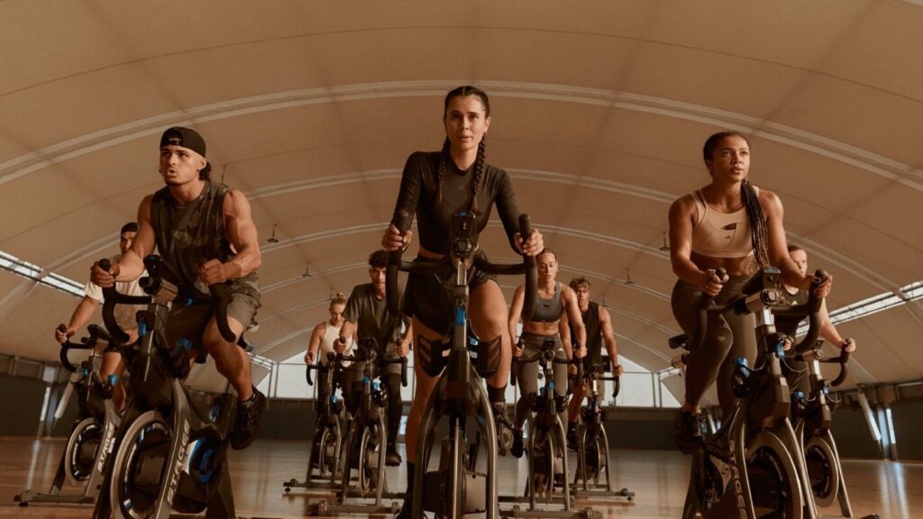 Groupe de sportifs en plein cours collectif de cardio sur vélo dans une salle de sport L’Appart Fitness, concentrés et motivés lors d’un entraînement RPM.