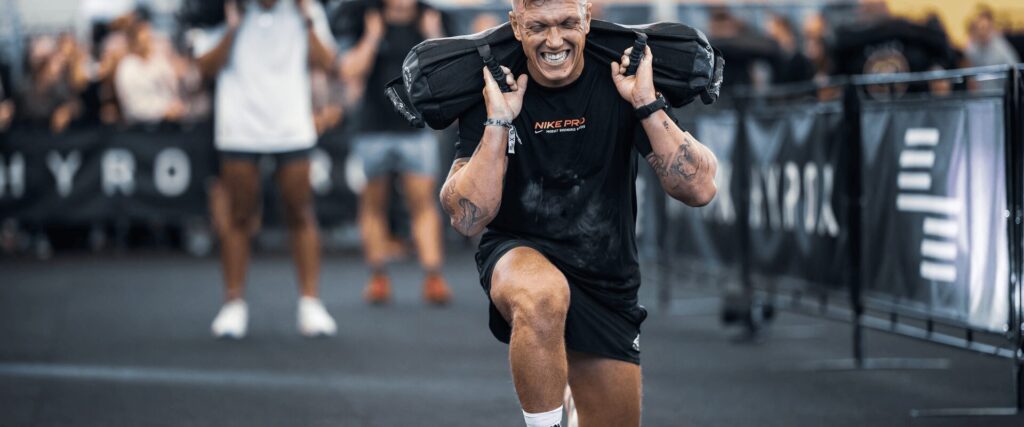 Sportif en pleine épreuve Hyrox avec sac lesté, durant un training intense à L’Appart Fitness.