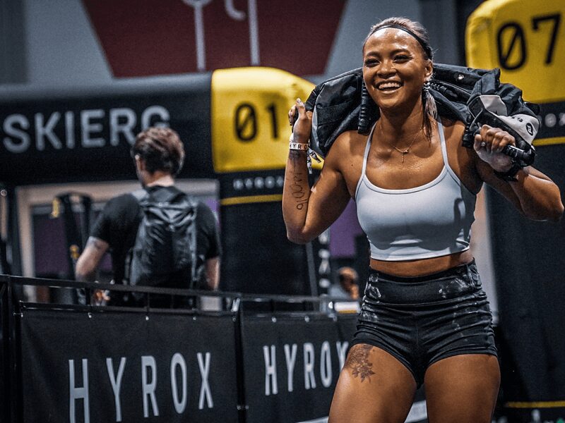 Athlète souriante en plein effort lors d'un entraînement Hyrox, organisé par L'Appart Fitness.