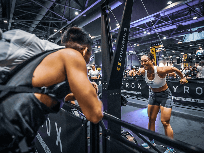 Séance d'entraînement Hyrox à L’Appart Fitness : effort intense sur le SkiErg sous les encouragements d’un partenaire.