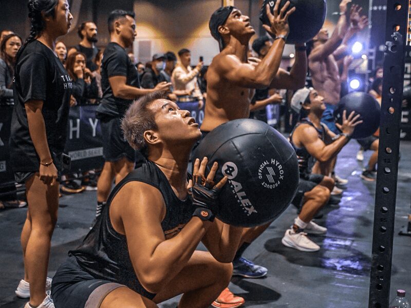Séance d'entraînement collective avec wall balls dans un événement Hyrox encadré par L'Appart Fitness.
