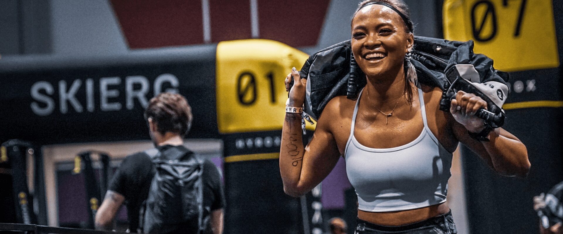 Athlète souriante en plein effort lors d'un entraînement Hyrox, organisé par L'Appart Fitness.