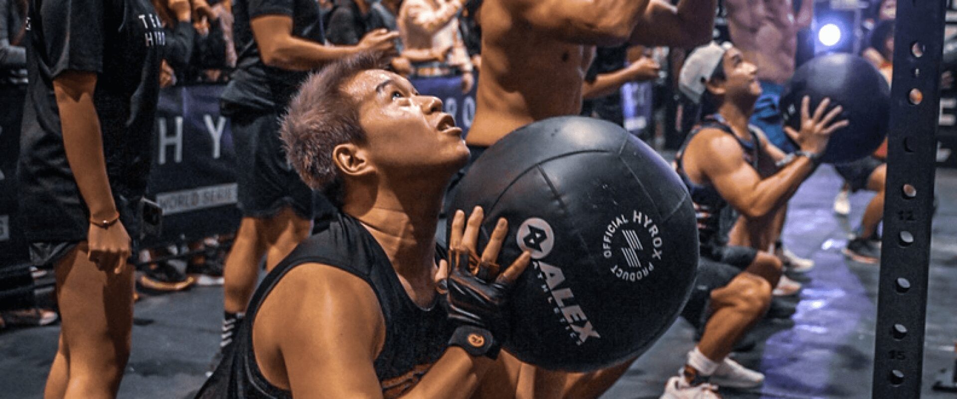 Séance d'entraînement collective avec wall balls dans un événement Hyrox encadré par L'Appart Fitness.