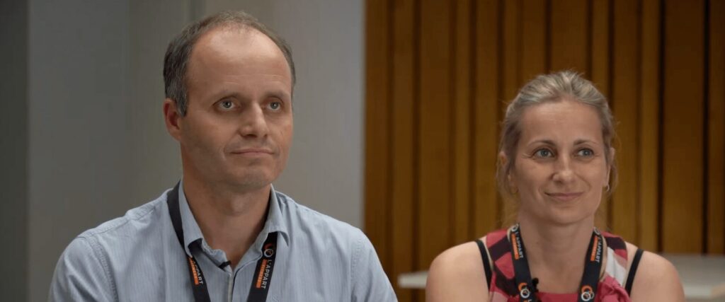 Portrait de Jimmy et Carine, tous deux souriants, portant le badge L’Appart Fitness. Un duo de en reconversion dans une franchise de salle de sport L'Appart Fitness Meylan.